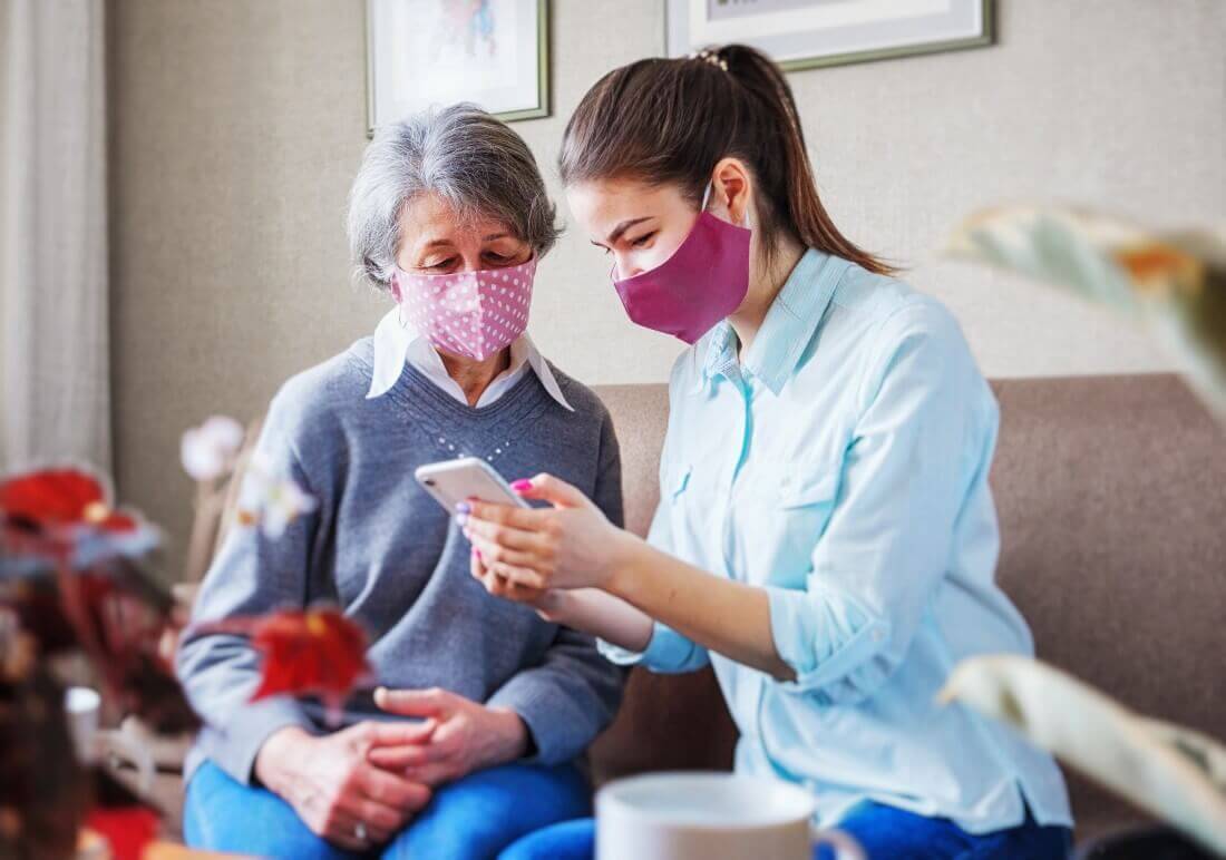 Caregiver and Senior Resident with Masks On Looking at Phone